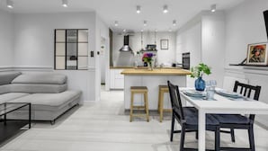 A modern kitchen with a central island, a dining area with a white table and chairs, and a grey sofa in a spacious living area.