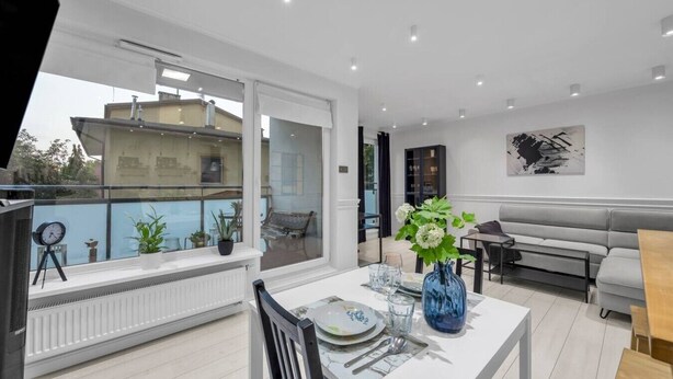 A modern living room with a dining area, a sofa, and a view of a building through a large window.