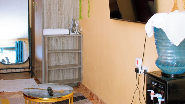 Quarto com armário de madeira, televisão fixada na parede, bebedouro e piso estampado.