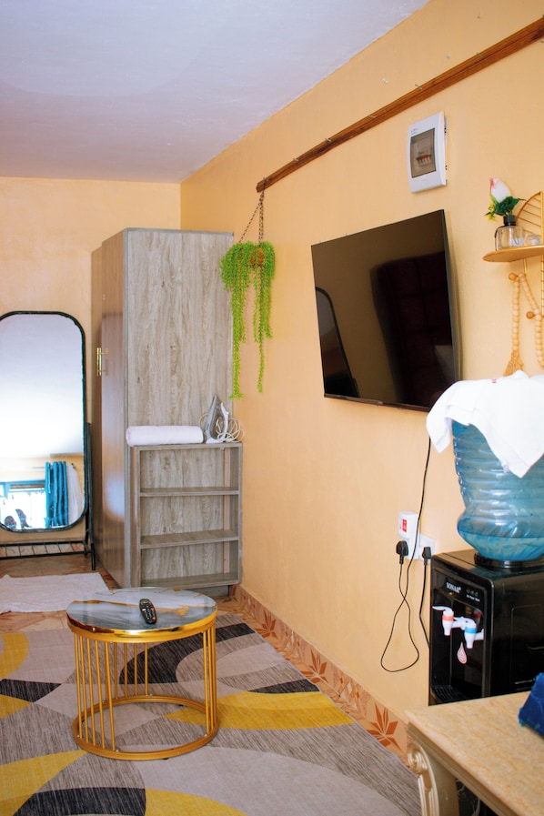 Une pièce avec un meuble en bois, un téléviseur fixé au mur, un distributeur d’eau et un sol à motifs.