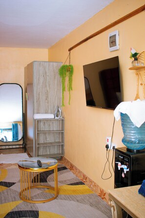 A room with a wooden cabinet, a television mounted on the wall, a water dispenser, and a patterned floor.