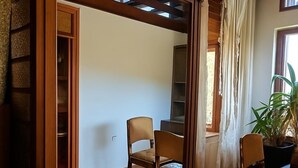 Um quarto com janela de madeira, duas cadeiras, um vaso de planta e uma estante de livros.