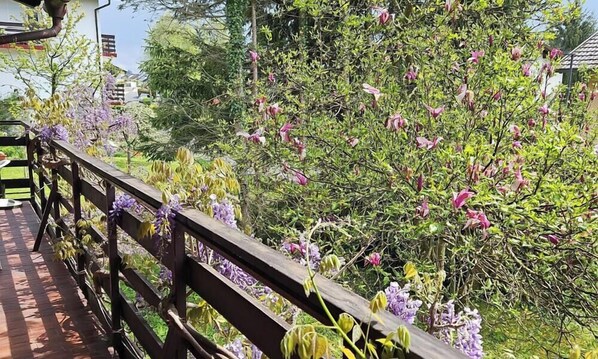 En træterrasse med gelænder, omgivet af frodigt grønt og blomstrende træer.