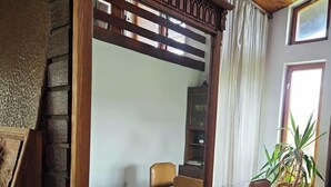 Um quarto com divisória de madeira, uma cadeira, uma estante de livros e um vaso com planta.
