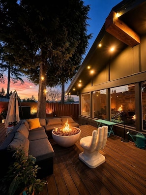 An outdoor deck with a fire pit, seating, and a view of the building's interior.