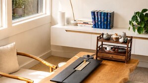 Een houten tafel met een dienblad, een stoel, een bank, een raam en een boekenkast met boeken en decoratieve objecten.