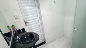 A bathroom with a black sink, white tiled walls, a glass shower enclosure, and a red bath mat. - Rooms for rent in Belém (Belém)