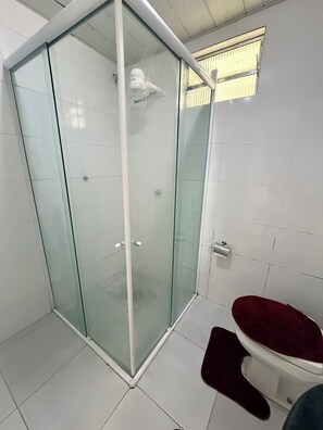 Un baño con cabina de ducha de vidrio, inodoro con asiento rojo y paredes cubiertas de azulejos blancos.
