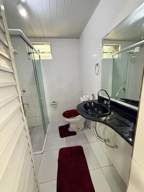Une petite salle de bain dotée d’une douche à parois de verre, de toilettes blanches, d’un lavabo noir et d’un tapis de bain rouge.