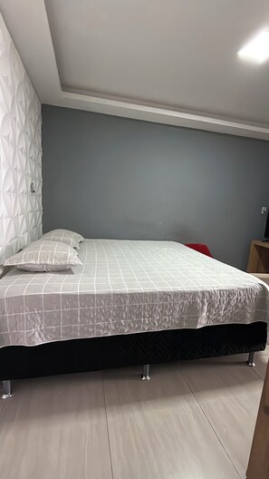 Camera da letto con un letto, una poltrona rossa, un comodino in legno e una lampada a parete.