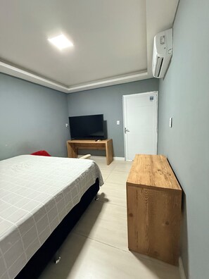 Una camera da letto con un letto, una TV su una scrivania in legno, un comodino in legno e un condizionatore d'aria a parete.
