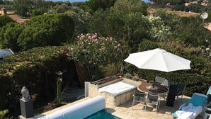 Una piscina con agua cristalina, rodeada por un solárium de piedra y un patio con mesa y sillas.