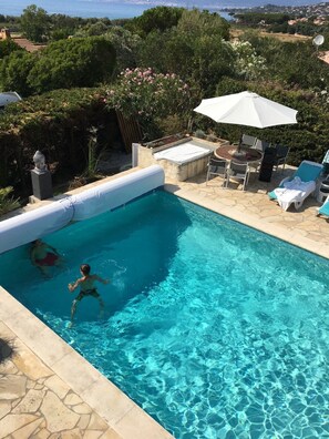 Ein Schwimmbecken mit klarem Wasser, umgeben von einer Steindeck und einer Terrassenanlage mit Tisch und Stühlen.
