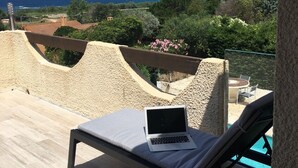 Un balcón con una computadora portátil, sillones de descanso y vistas al mar y a las montañas.