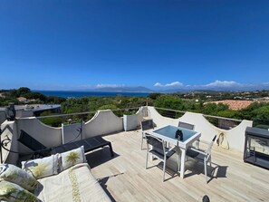 Eine Dachterrasse mit Tisch und Stühlen, einer Sitzecke und Blick auf das Meer und die Berge.