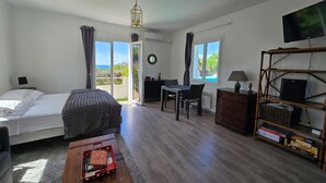 Una habitación con cama, escritorio, silla, televisor y vista al exterior.