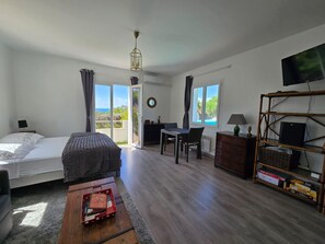 Ein Zimmer mit einem Bett, einem Schreibtisch, einem Sessel, einem Fernseher und Blick ins Freie.