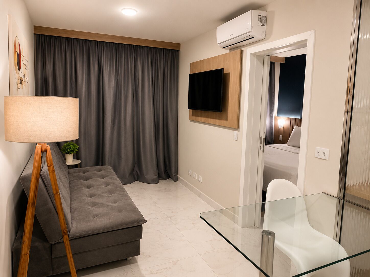 A modern room with a sofa, a glass table, a lamp, a TV, and an air conditioning unit.