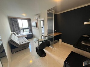 A modern room with a glass dining table, a sofa, a black chair, a black countertop, and a sliding door.