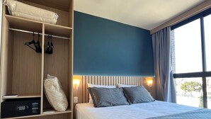 Een hotelkamer met een bed, een kledingkast, een bedieningspaneel en een raam met gordijnen.
