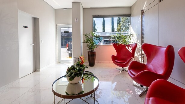 Een moderne lobby met een glazen tafel, rode stoelen, een potplant en een groot raam.