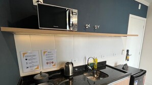 Een moderne keuken met een magnetron, waterkoker, spoelbak en een koelkast.