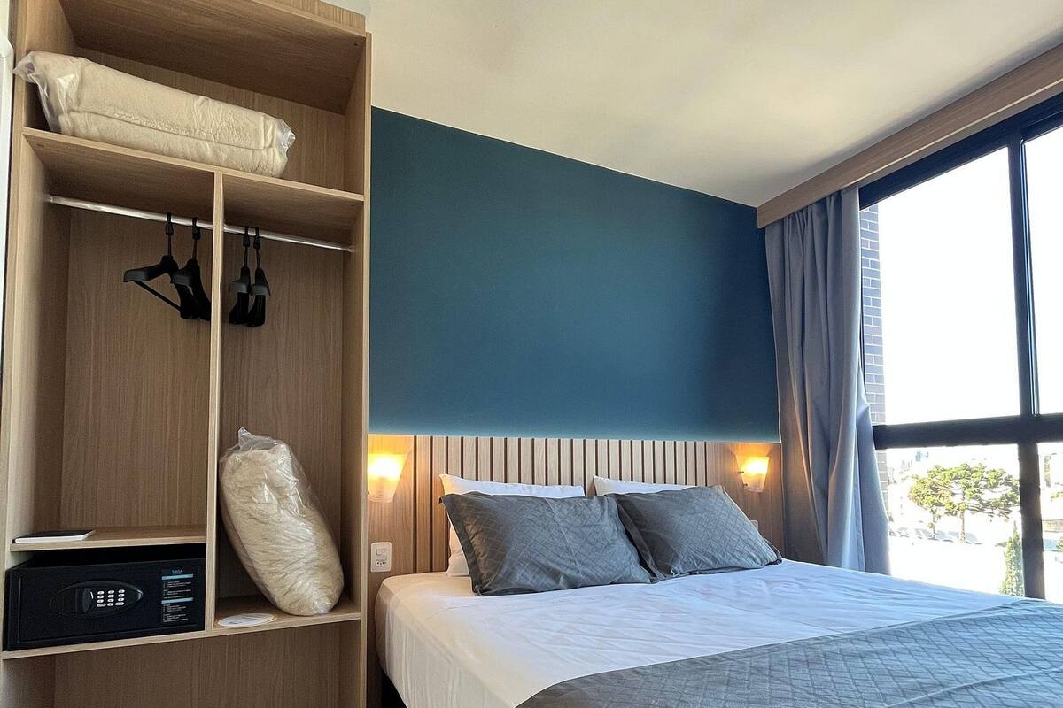 A hotel room with a bed, a wardrobe, a control panel, and a window with curtains.