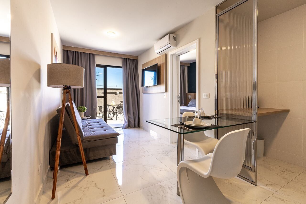 A modern hotel room with a glass dining table, a sofa, a lamp, and a TV.