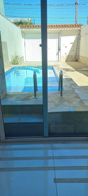 A swimming pool with a tiled deck, a metal railing, and a door leading to a covered area.
