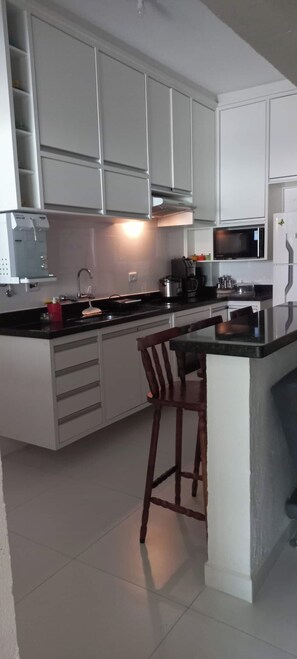 Eine moderne Küche mit weißen Schränken, einer schwarzen Arbeitsplatte, einer eingebauten Mikrowelle und einer Kaffeemaschine.