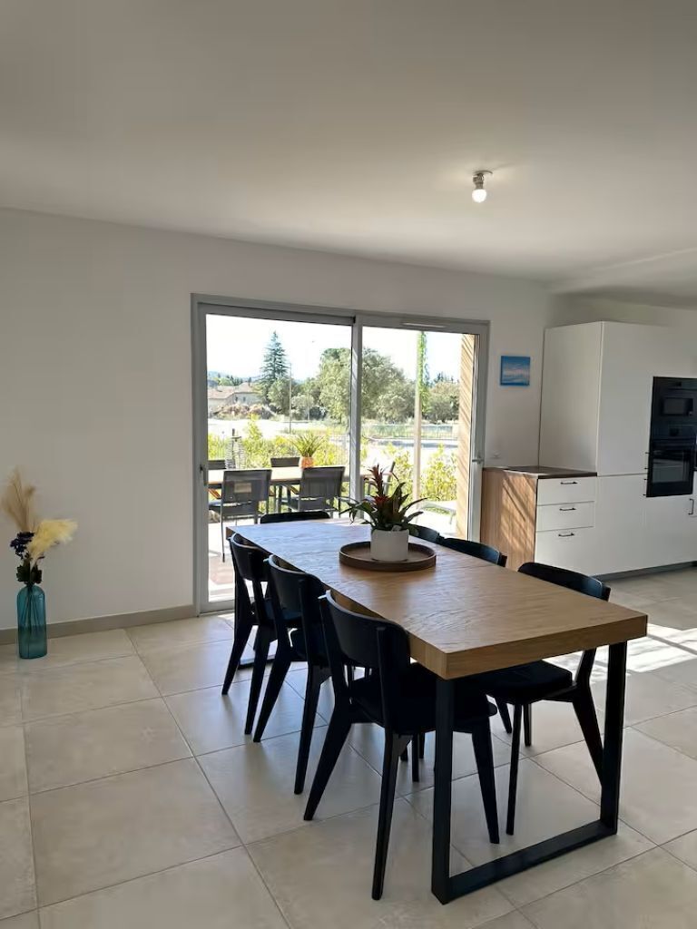 Une cuisine moderne avec des meubles blancs, un four encastré et un coin repas comprenant une table en bois et des chaises noires.