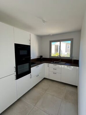 Een keuken met witte kastjes, een zwarte oven, een raam met uitzicht en een betegelde vloer.
