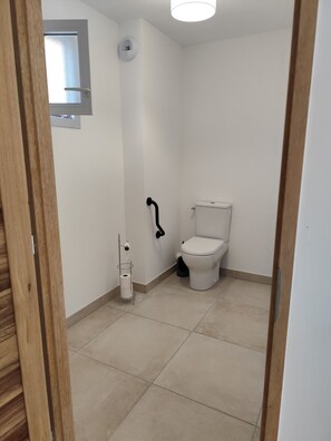A small, clean bathroom with a toilet, a handrail, and a window. - LE SOLEIL DU GOLF PMR Sud (Saumane-de-Vaucluse)