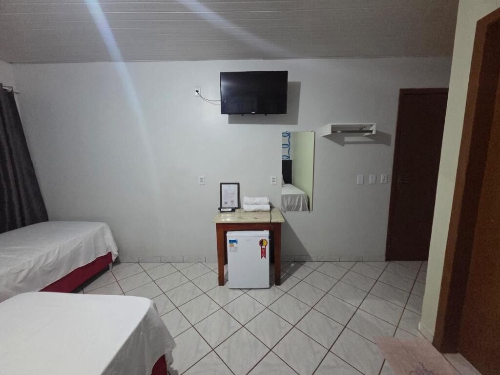 Habitación de hotel con dos camas, una mesita con refrigerador, televisión montada en la pared y una puerta a la derecha.