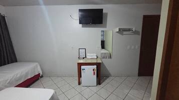Habitación de hotel con dos camas, una mesita con refrigerador, televisión montada en la pared y una puerta a la derecha.