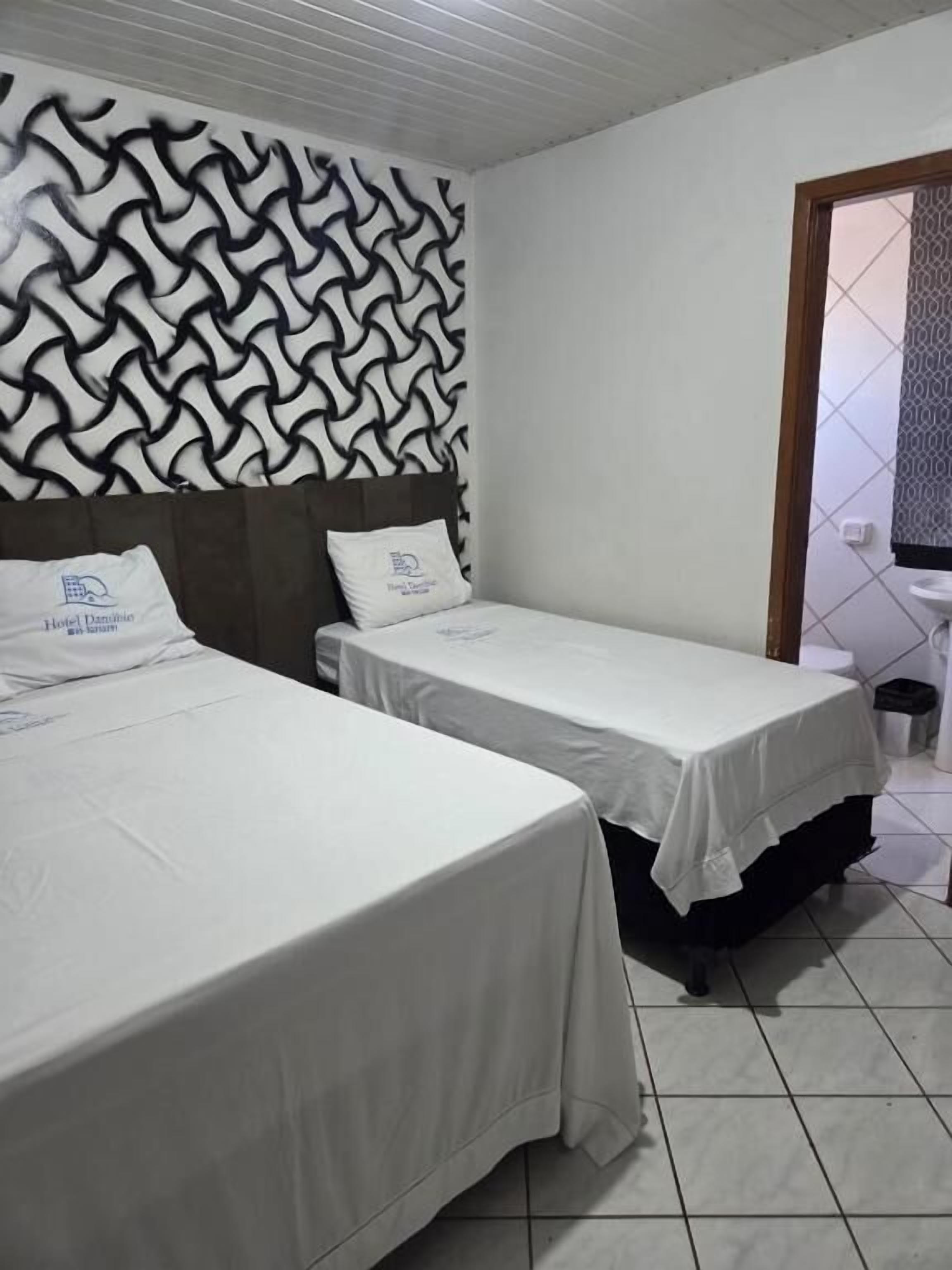 Habitación de hotel con dos camas, un papel tapiz estampado, un lavamanos y suelo de baldosas.