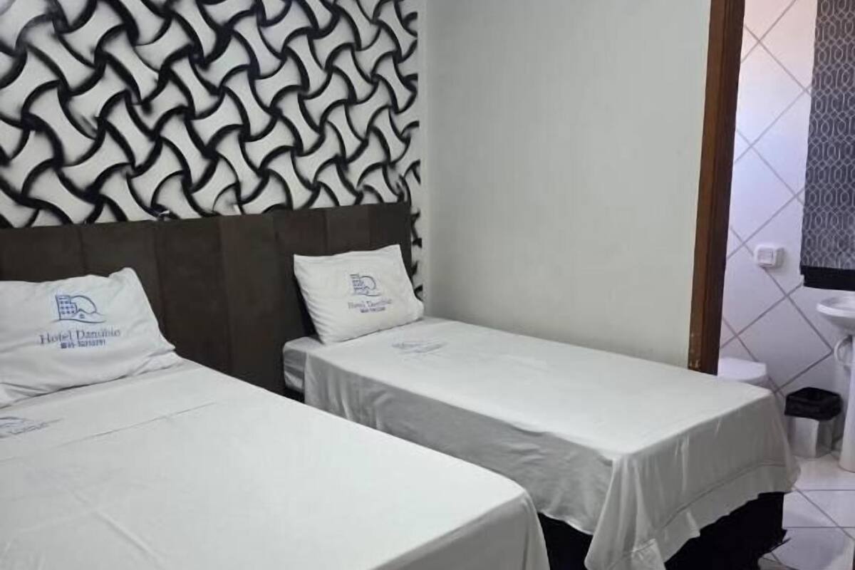 Habitación de hotel con dos camas, un papel tapiz estampado, un lavamanos y suelo de baldosas.