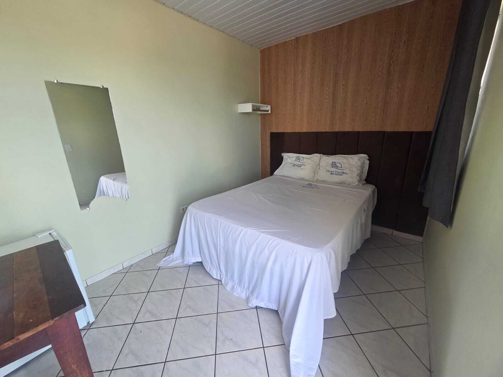 Una habitación de hotel con una cama, una mesita pequeña, un espejo y un cabecero de madera.
