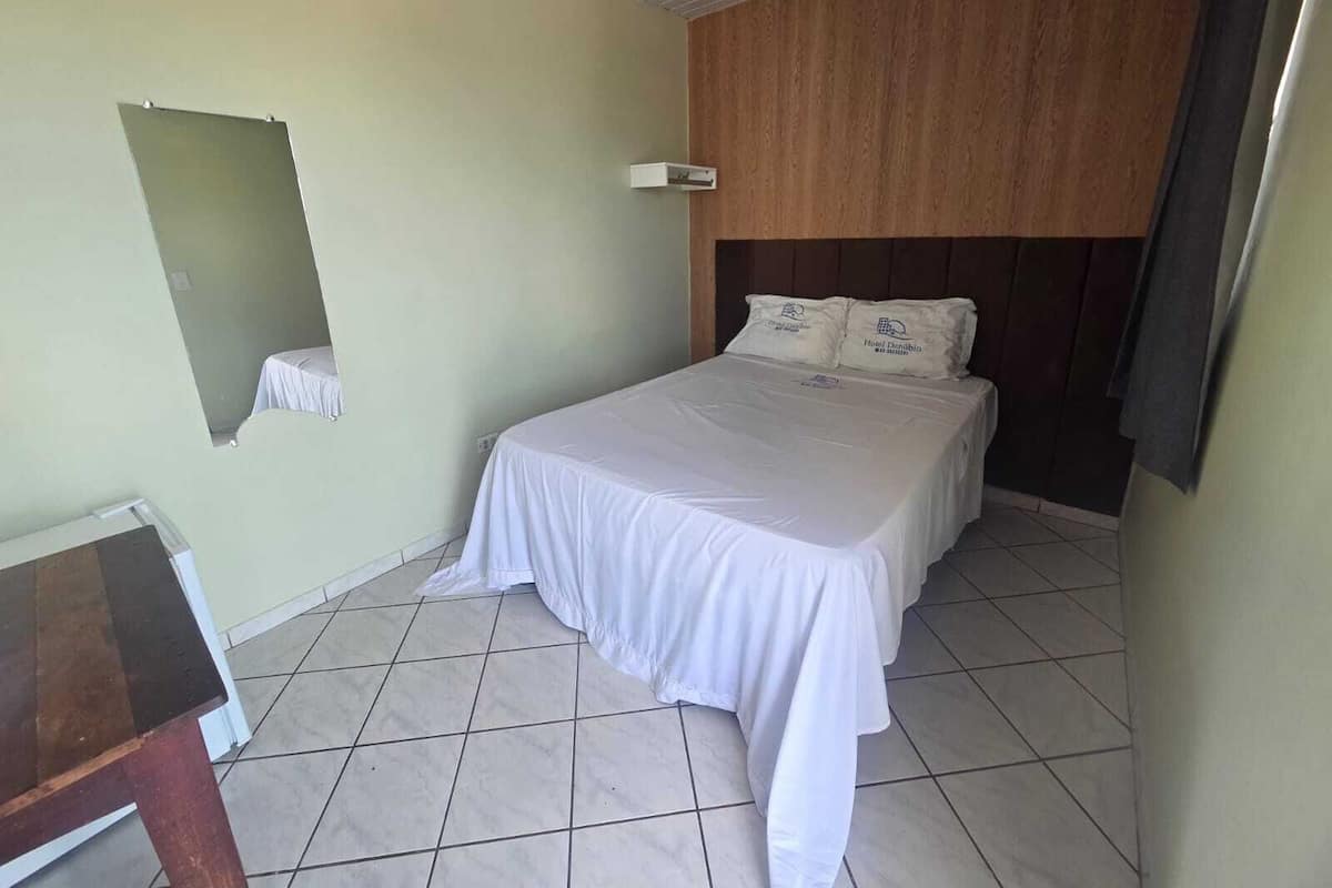 Una habitación de hotel con una cama, una mesita pequeña, un espejo y un cabecero de madera.