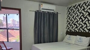 Habitación de hotel con dos camas, una ventana con cortinas, un aire acondicionado y vistas a edificios.