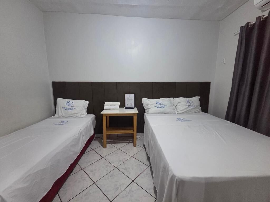 Habitación de hotel con dos camas individuales, una mesita de noche pequeña, aire acondicionado de pared y una cortina a la derecha.