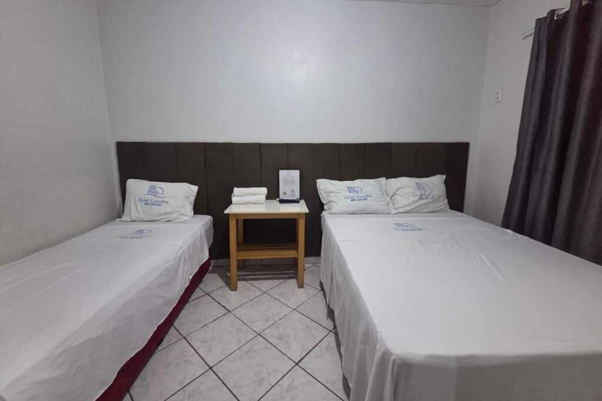 Habitación de hotel con dos camas individuales, una mesita de noche pequeña, aire acondicionado de pared y una cortina a la derecha.