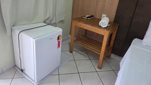 Una habitación pequeña con un refrigerador blanco, una mesa de madera con una toalla y una cama.