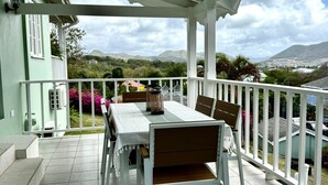 Een overdekt terras met een tafel en stoelen, een witte balustrade en uitzicht op het omliggende landschap.