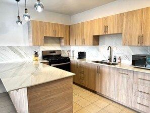 Una cocina moderna con armarios de madera, encimera de mármol, estufa negra y un lavabo.