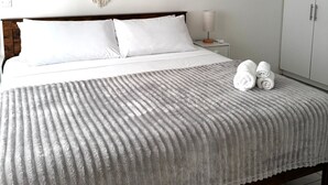 Een slaapkamer met een bed, witte beddengoed, macramé wanddecoratie en een kledingkast.