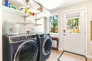 A laundry area with two front-loading washers, a basket, and shelves with various items. - 4BR Wellness Retreat Hot Tub, Sauna & Game Room (Nekoosa)