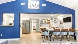 A modern kitchen with stainless steel appliances, a dining area with patterned chairs, and a blue accent wall with a 'NILD' sign. - 4BR Wellness Retreat Hot Tub, Sauna & Game Room (Nekoosa)