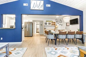 A modern kitchen with stainless steel appliances, a dining area with patterned chairs, and a blue accent wall with a 'NILD' sign. - 4BR Wellness Retreat Hot Tub, Sauna & Game Room (Nekoosa)