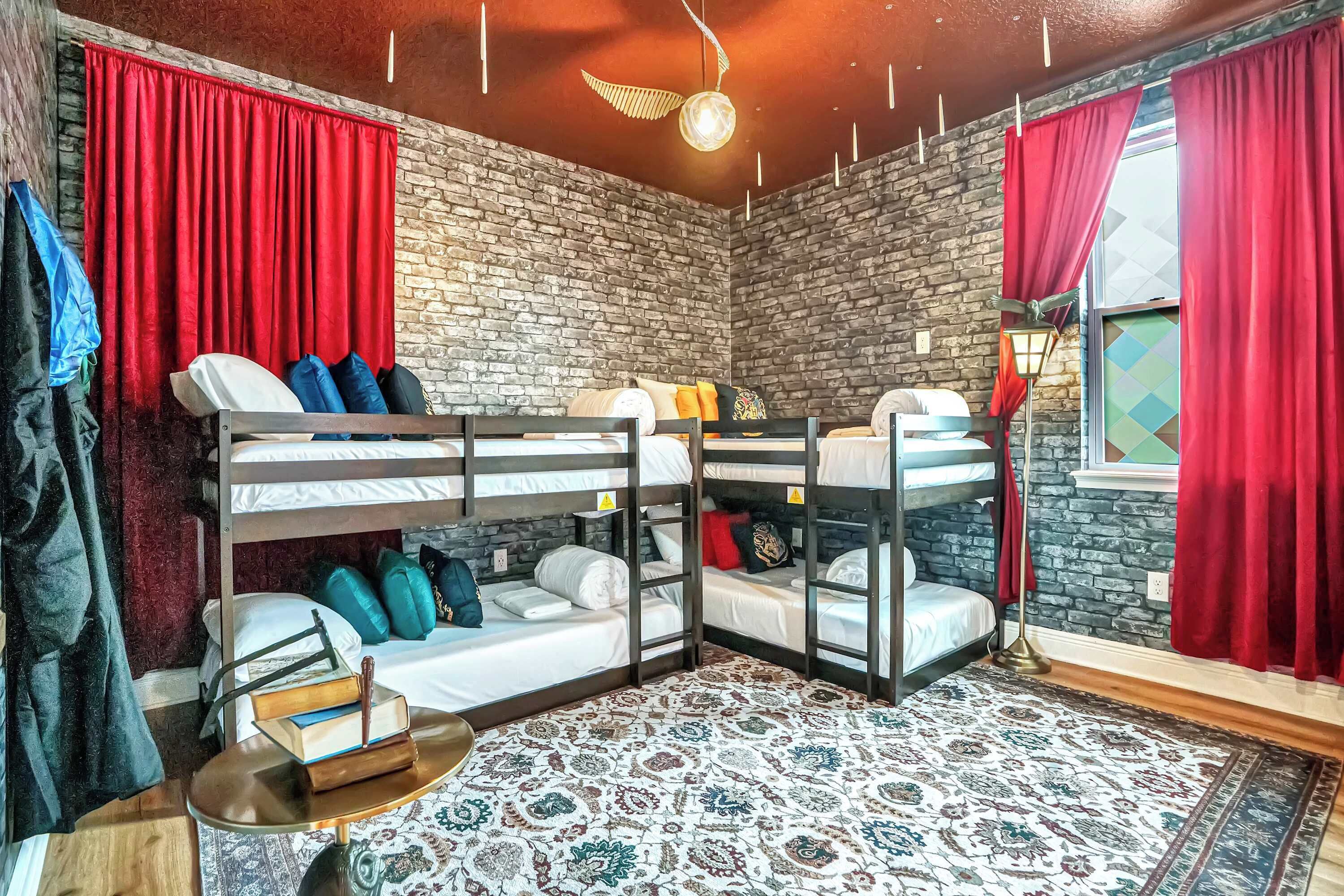 A room with bunk beds, a patterned rug, a round table with books, and a brick wall.